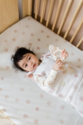 baby in crib wearing sleep bag and holding teething ring