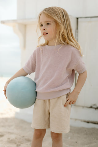 A young blond girl wearing Towel Terry holds a beach ball.