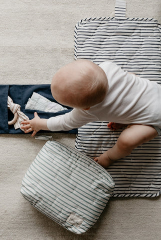 toddler sitting on portable changing pad reaching for diaper