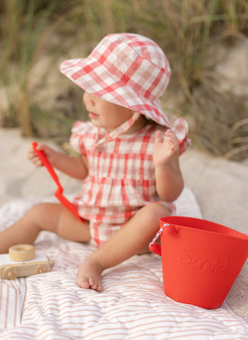 Toddler in CheckMate clothing and Bucket Hat sitting on Play Mat at the beach