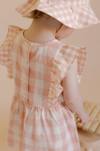 A girl is smiling at the camera, wearing a Checkmate Flutter Dress and Bucket Hat.