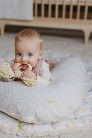 A baby lies on a Pehr nursing pillow with an On The Go teether.