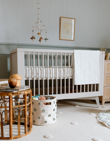 An image of a nursery with a crib and wicker ottoman.