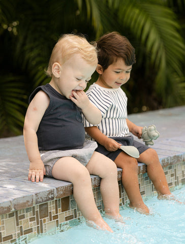 Toddler boys in summer outfits sitting on edge of pool