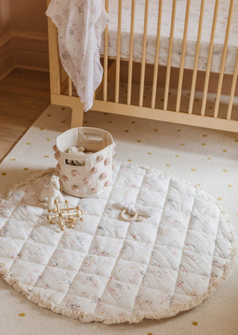 Image of a nursery with a play mat, pom pom pint, swaddle and crib sheet.