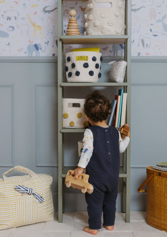 Child reaching for Pehr Pom Pom Storage on shelf in nursery