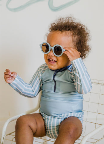Baby sitting on chair wearing sunglasses and Pehr Swimsuit