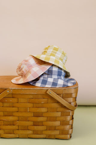 Three Checkmate Bucket Hats are stacked on a picnic basket.