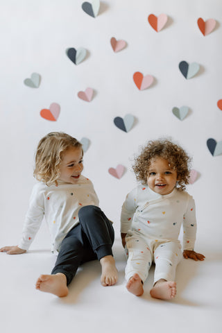 A little boy and girl sit on a backdrop, decorated with hearts, in Pehr Valentine’s clothes.