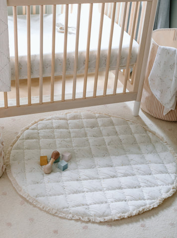 A nursery image with a crib, play mat and striped hamper.