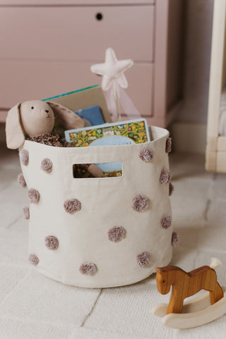 An image of a pom pom storage bin full of books and toys.