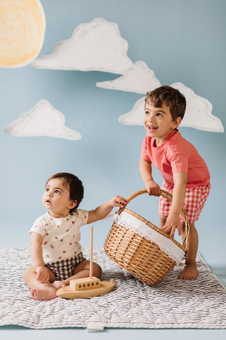 baby and toddler playing on striped play mat with basket and boat