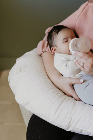 mother feeding newborn bottle on nursing pillow