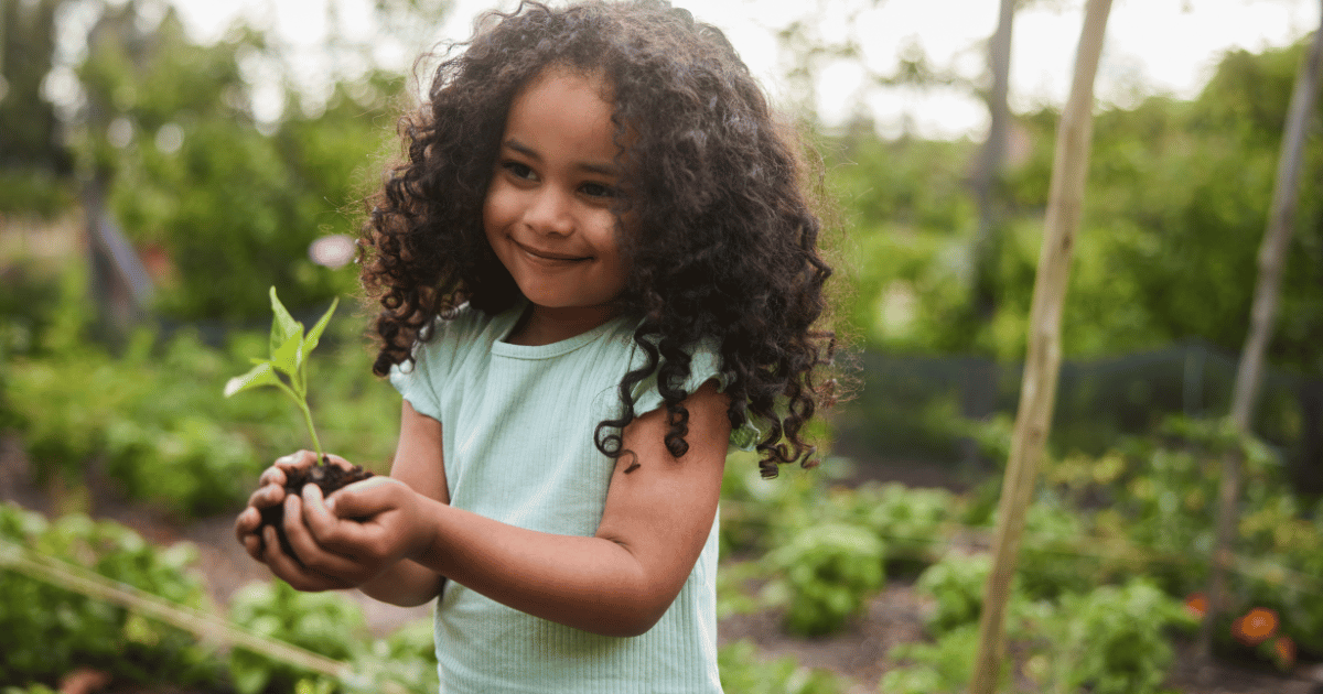 Little girl smiling holding a seedling in her hands.