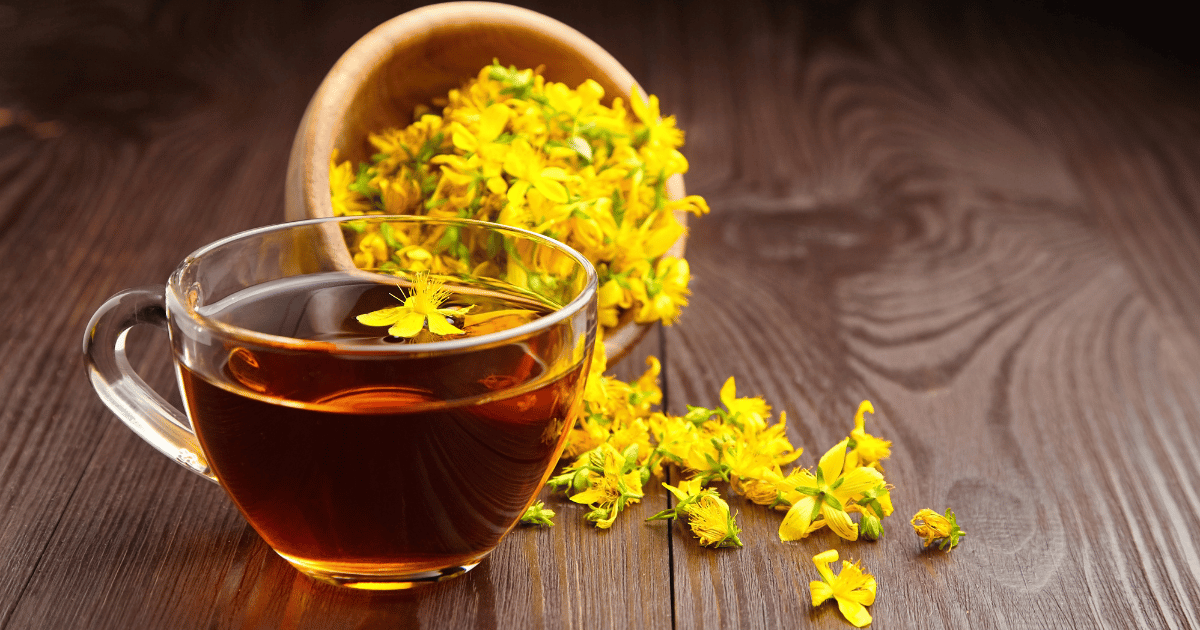 St John's Wort petals in a bowl spilling on a table with a cup of St John's Wort tea