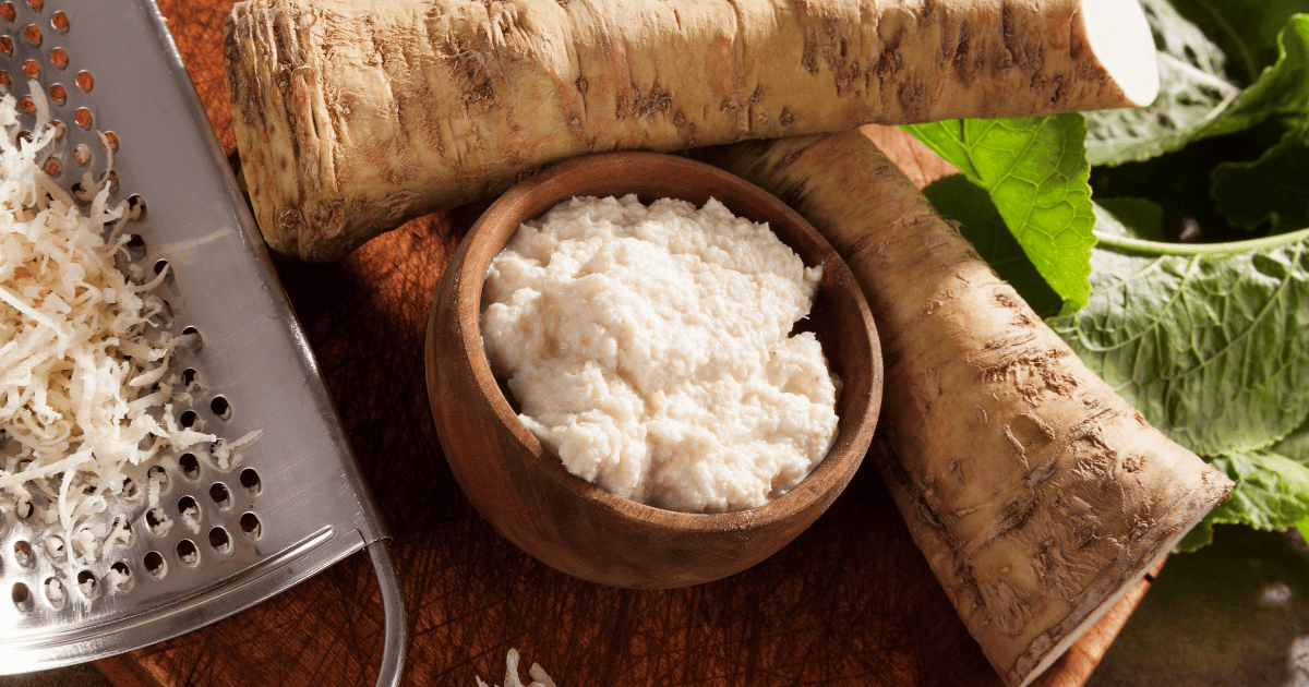 Fresh and grated horseradish with leaves on a wooden background.