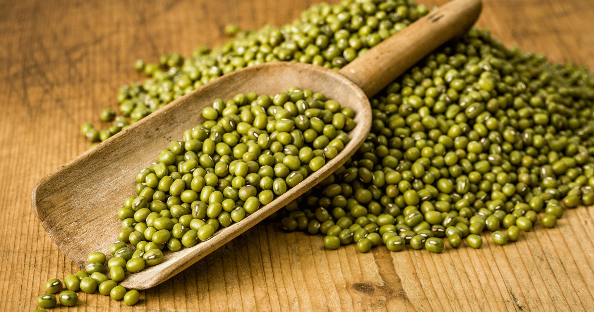 Mung beans in a wooden spoon on a wood table.