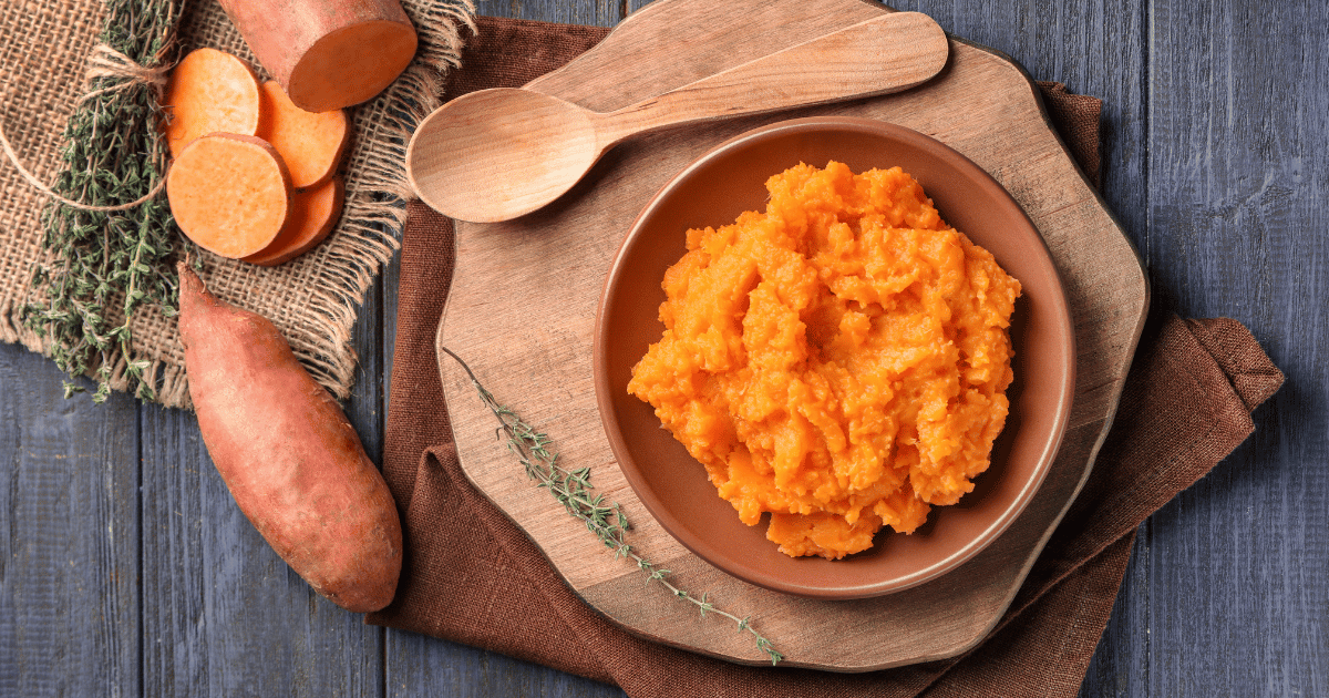 Sweet potatoes in bowl with a wooden spoon.