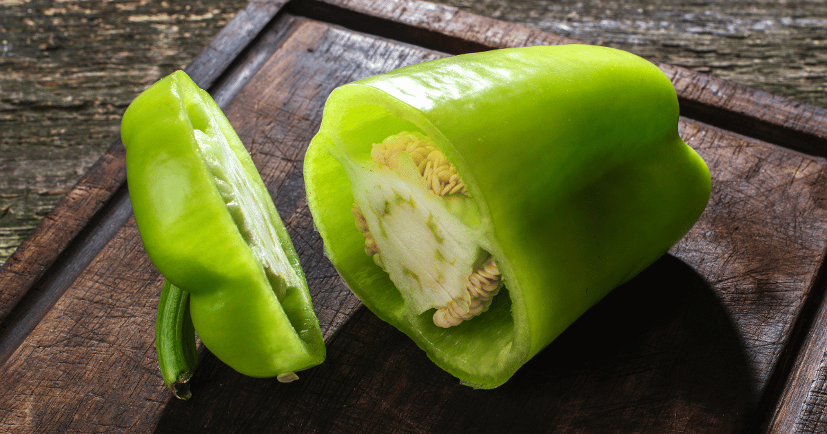 Sliced green bell pepper on a wooden cutting board and wood background.