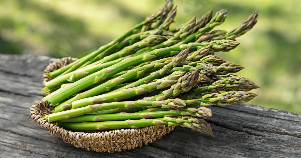 Asparagus in a small basket on a wooden table.