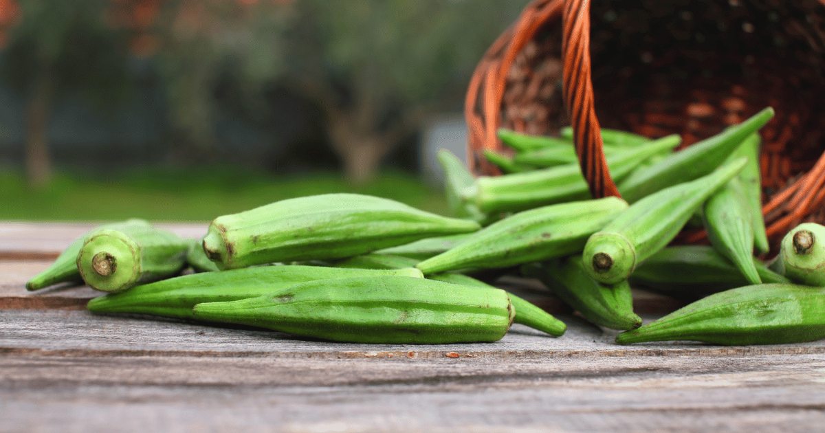 Okra spilling out of a basket onto a wooden background.