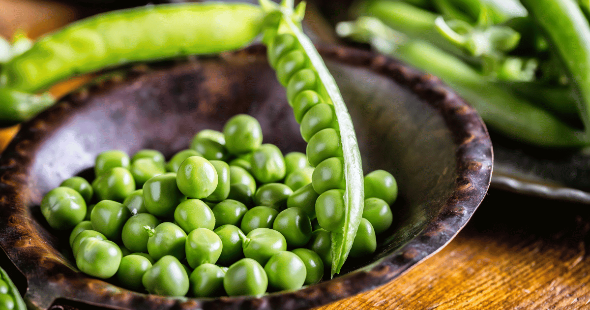 Fresh peas in a rustic bowl on a wooden table.