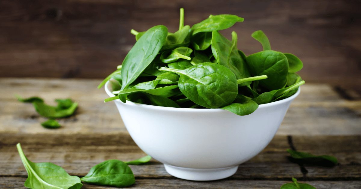 Baby spinach leaves in a white bowl on a wooden background.