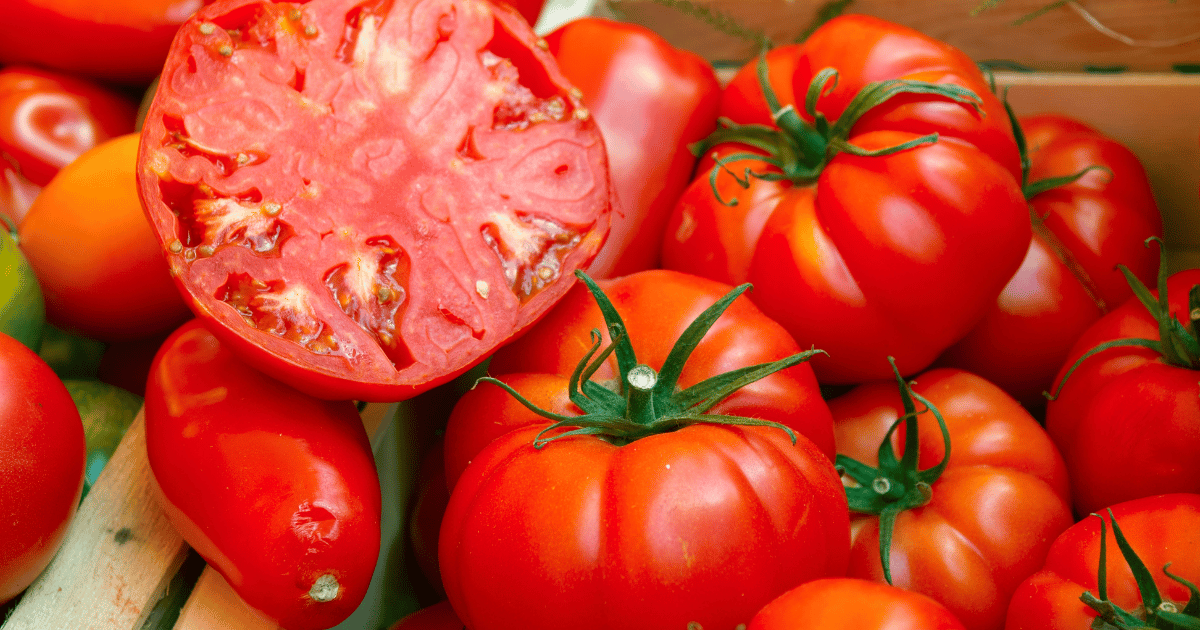 Sliced ripe beefsteak tomato at a market next to san marzano tomatoes.