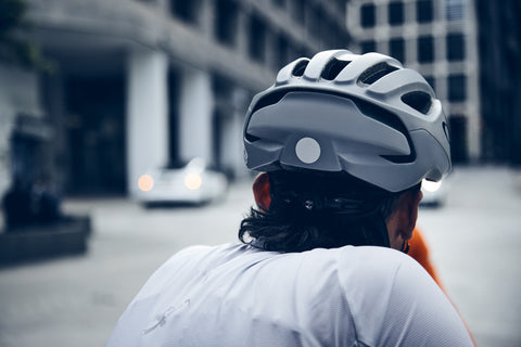 head of a cyclist with gray helmet seen from behind; the helmet has a reflective sticker on it