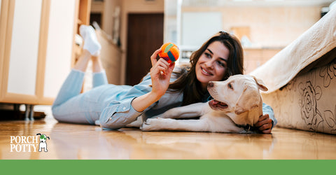 A woman with long dark hair lays down on the floor with her dog