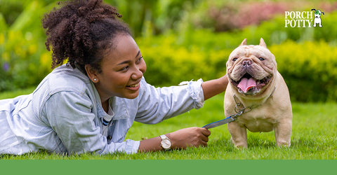 A tan bulldog and its owner lay down on the grass in a yard