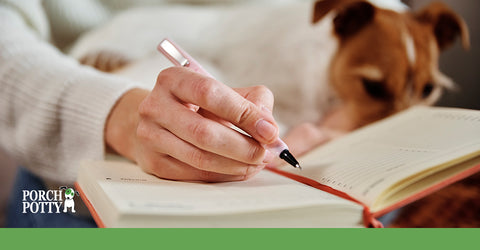 A Jack Russell Terrier's owner's hand writes in a notebook