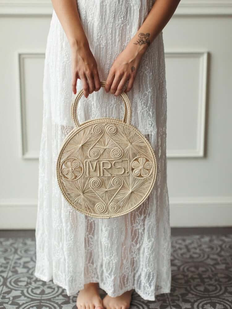 a model holding a beige woven “Mrs.” handbag