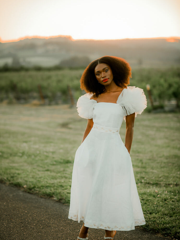 model in white puffy sleeve dress in front of a vineyard