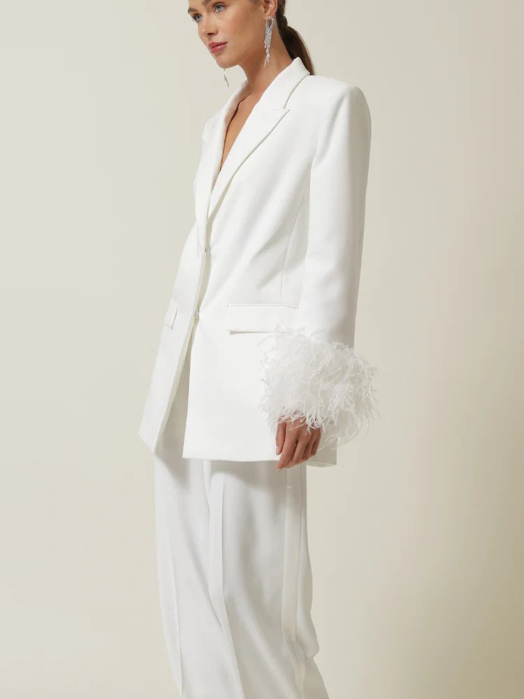 a model wearing a white blazer and pants set with feather cuffs