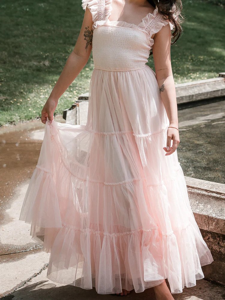 a model wearing a light pink tulle tiered maxi dress outdoors