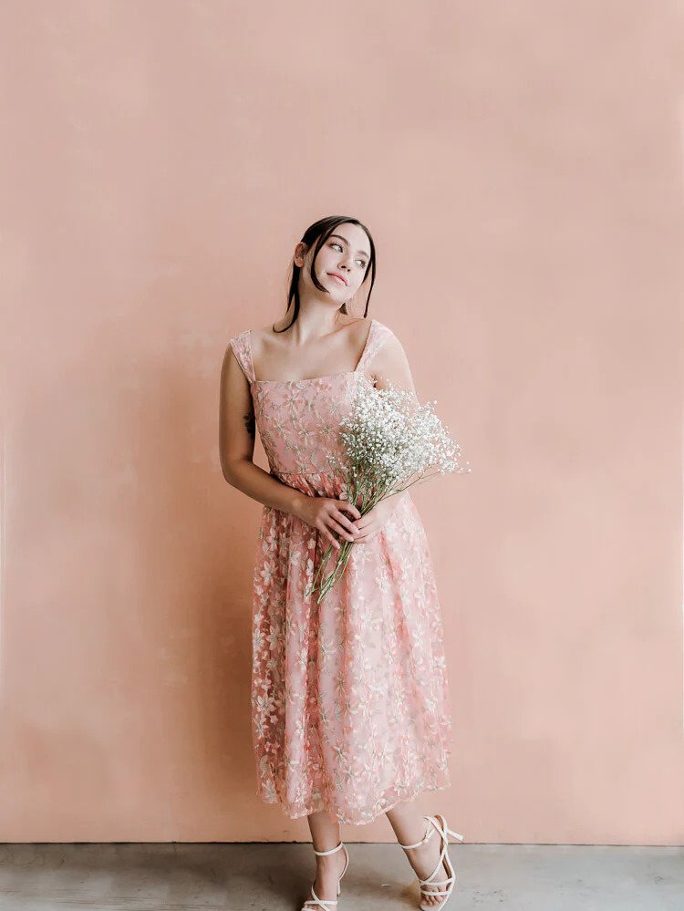 a model wearing a pink jacquard midi dress holding a white bouquet