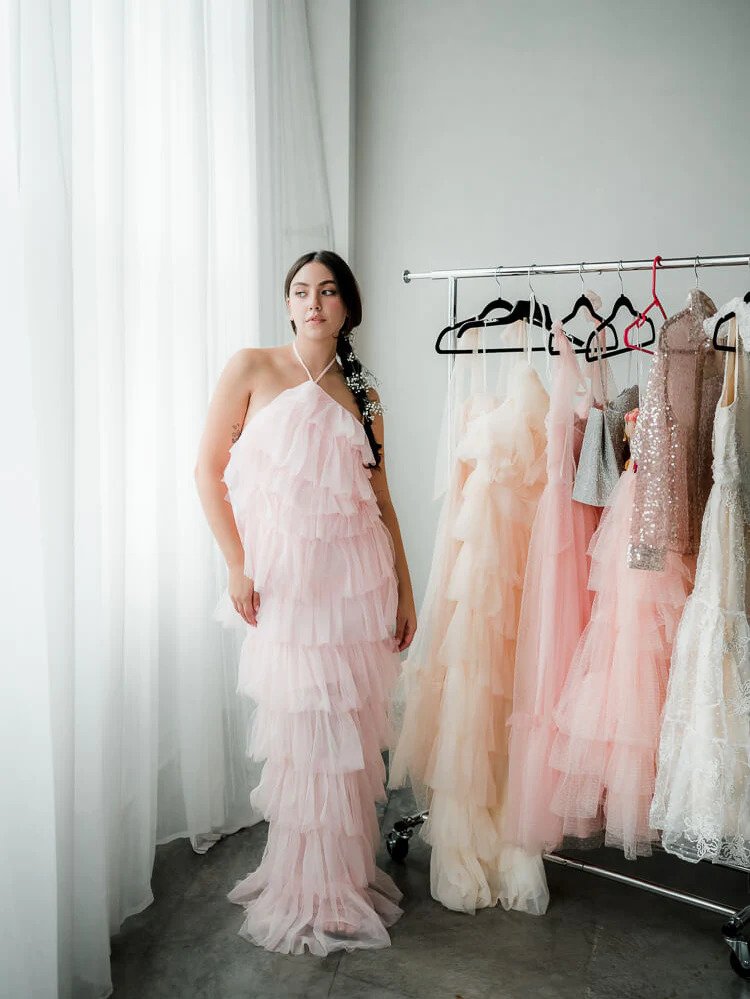 a model wearing a pink tulle halter midi dress beside a rack of similar styles