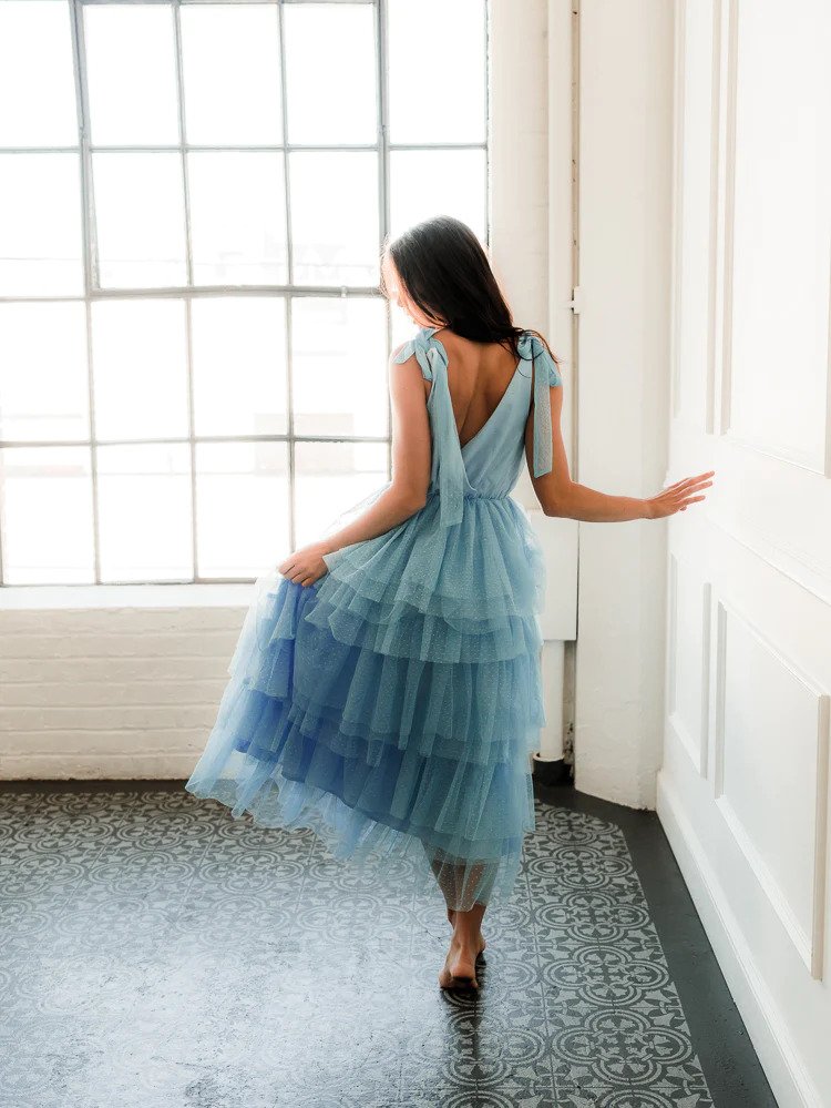 a model wearing a tiered blue tulle midi dress facing away from the camera