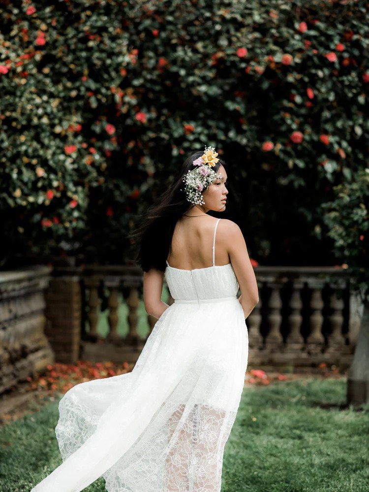 a model in a grassy yard wearing a lace wedding dress and a flower crown