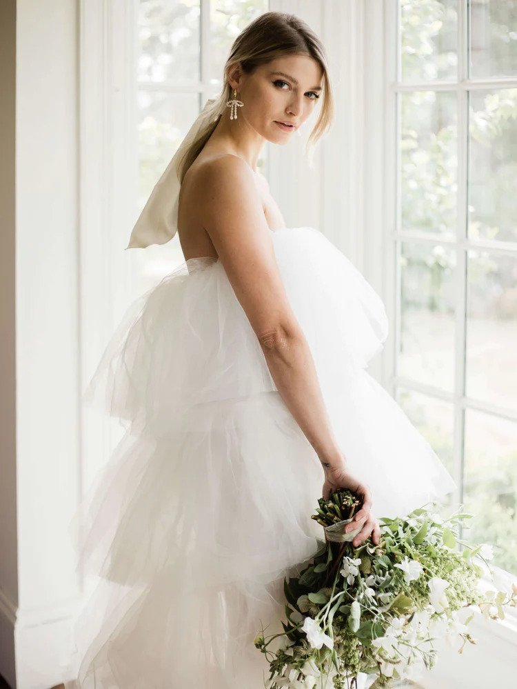 a model holding a white bouquet and wearing a dramatic tulle wedding dress