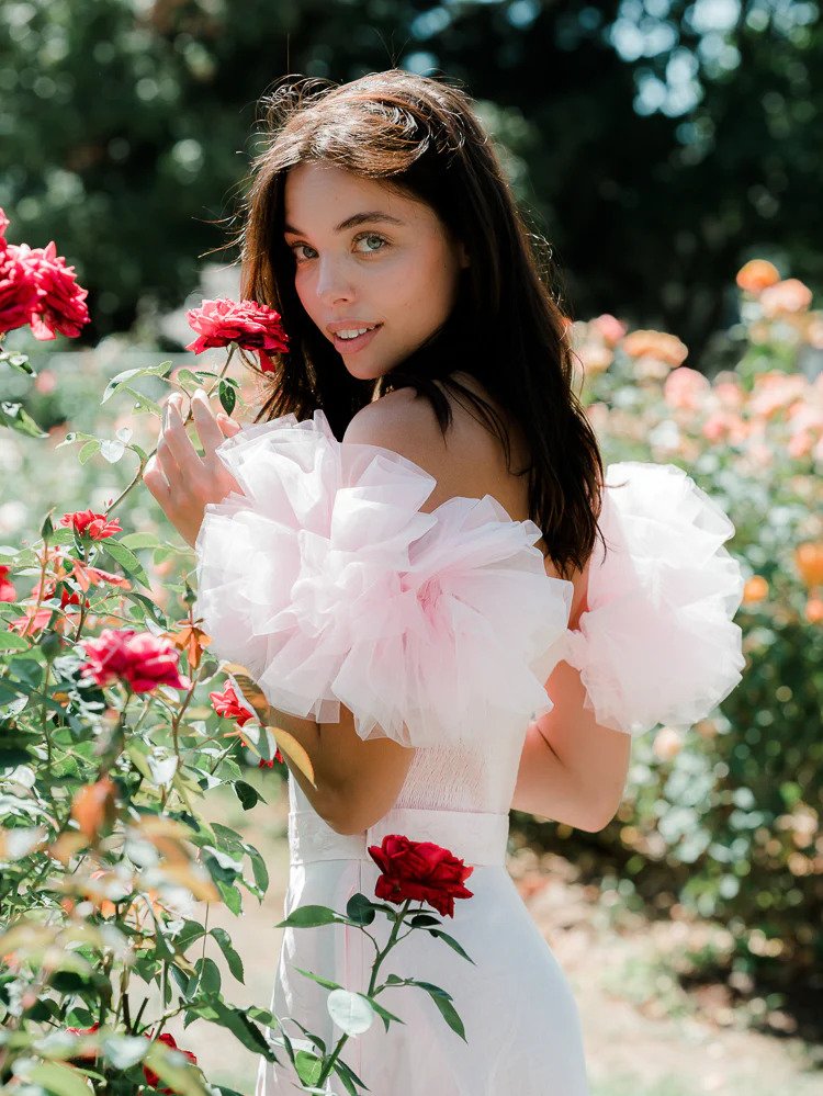 a model in a field of flowers wearing a pink tulle-sleeved dress