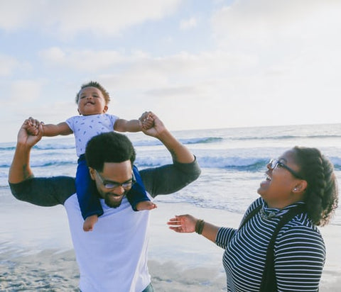 two adults and a toddler laughing on the beach for mothers day