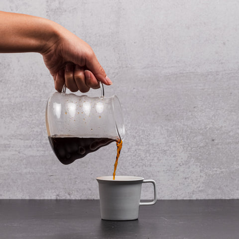 Coffee is poured from a glass carafe to a white cup.