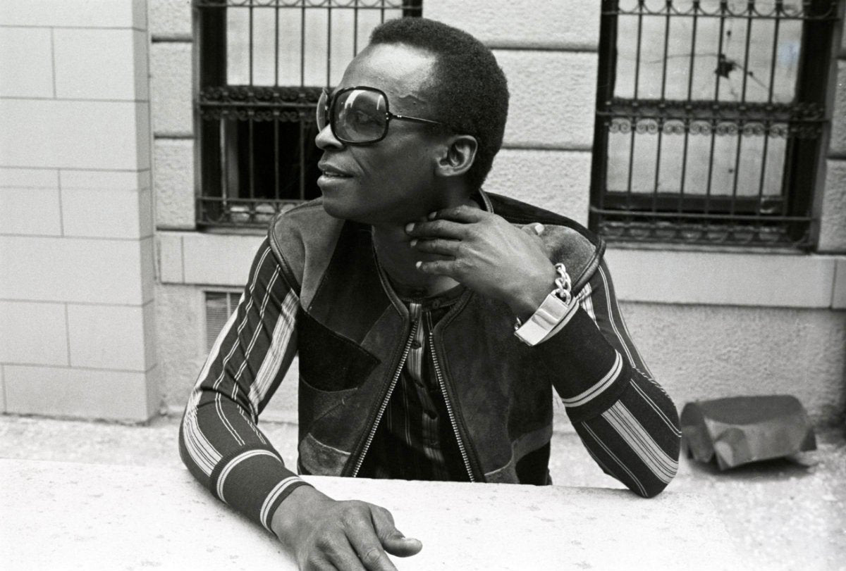 An extremely cool man in sunglasses and a striped jacket looks to his right. It's Miles Davis.