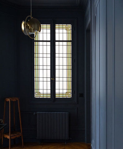 French window with white stained-glass, surrounded by dark blue walls and silver lamp hanging from the ceiling.
