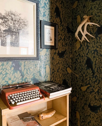 Corner of a room with birds wallpaper and wooden table with typewriter on top.