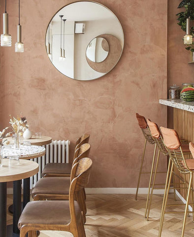 Dusty pink wall with mirror, room with wooden chairs and tables.