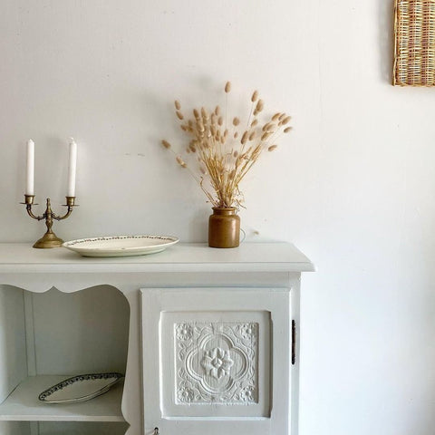 White wall, light colored chest with floral details.