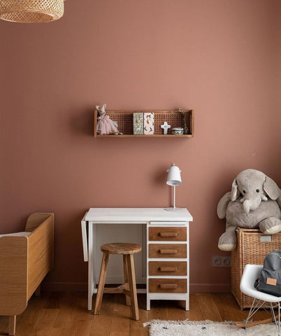 Children's room with dusty pink walls and small white table with wooden stool.